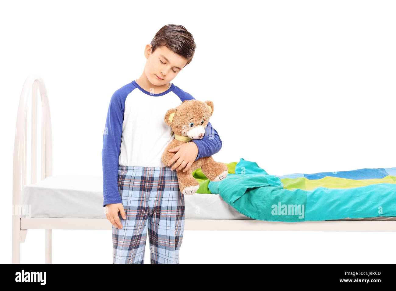 Sleepy boy holding a teddy bear et debout devant un son lit isolé sur fond blanc Banque D'Images