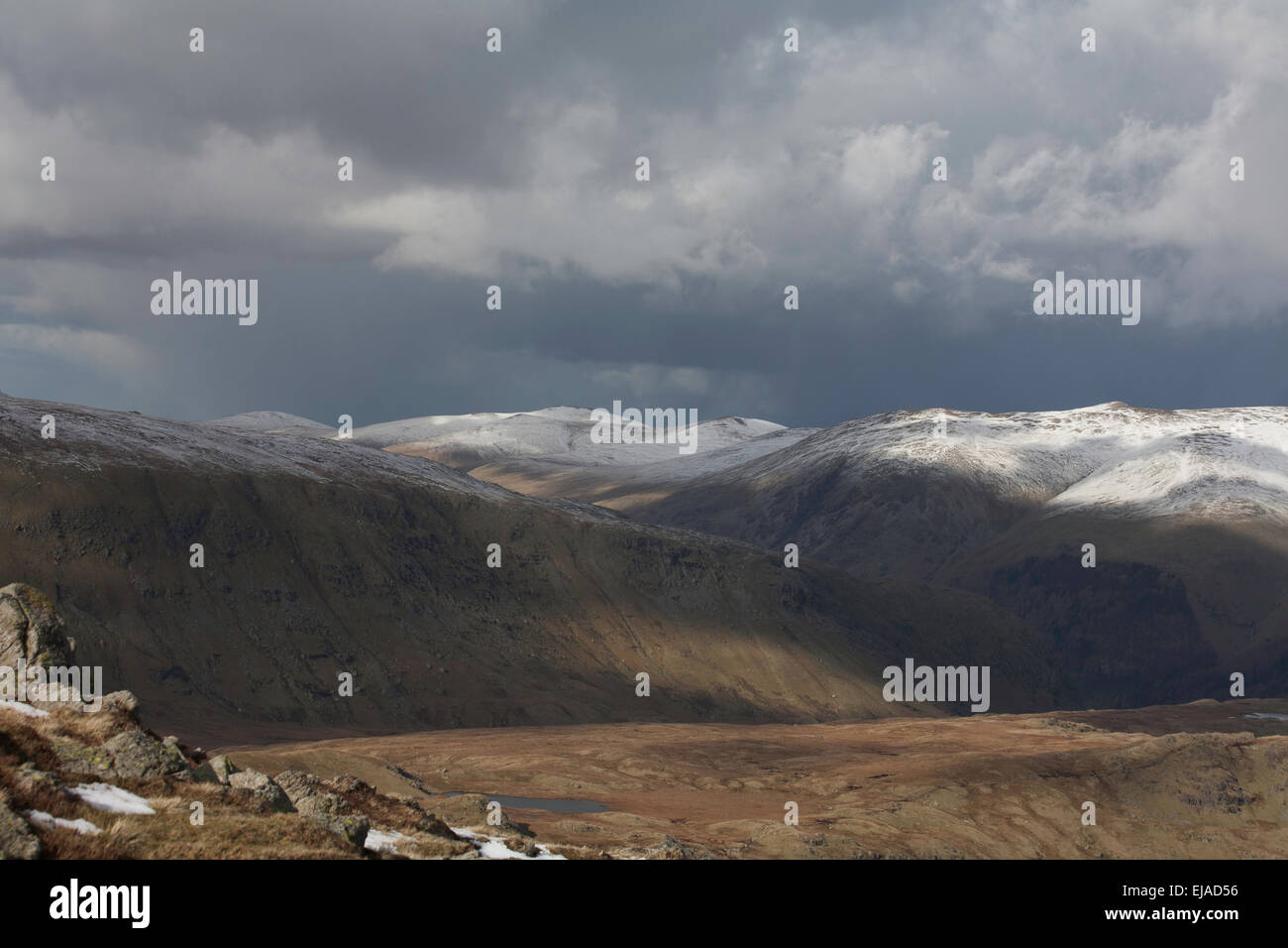 Storm & douche nuages passant au-dessus du sommet enneigé de Helvellyn de cendres sur les rochers près de soulever haut au-dessus de Grasmere Cumbria Banque D'Images