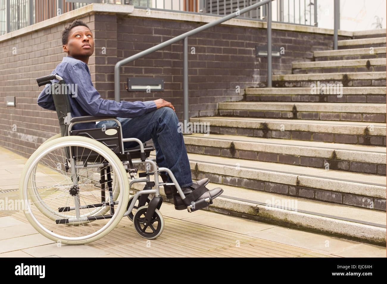 Jeune homme en fauteuil roulant en attente d'aide au bas d'un escalier. Banque D'Images