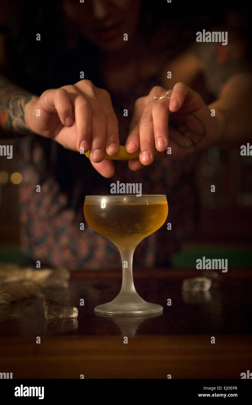 Les mains d'une femme serrant une tranche de citron dans un verre à cocktail. Banque D'Images