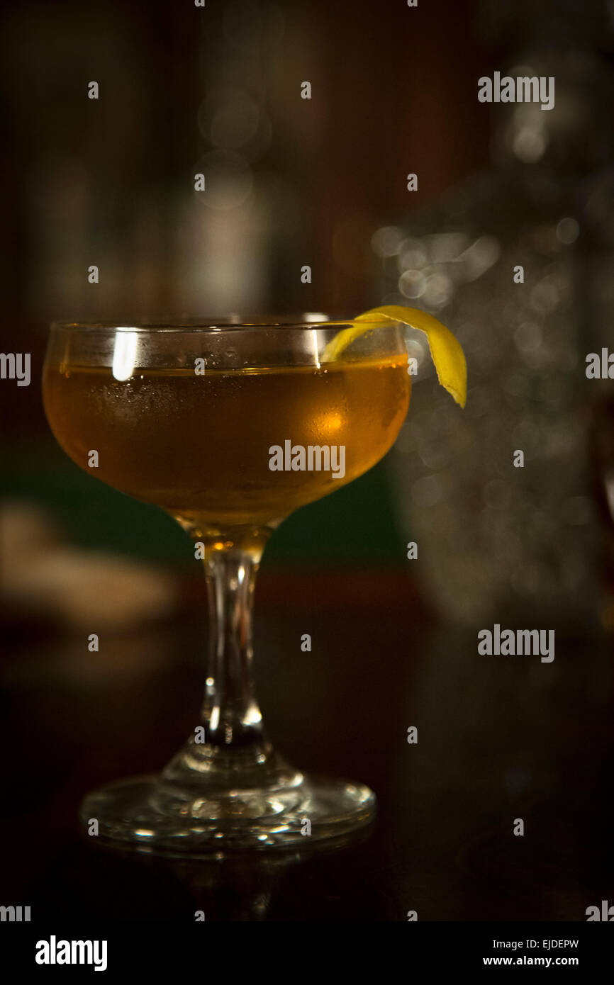Un verre à cocktail avec un cocktail et le zeste de citron en appui sur le bord. Banque D'Images