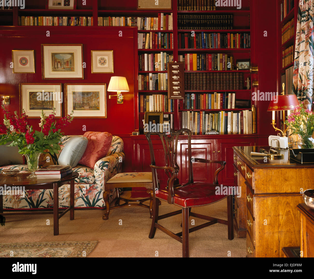 Photos sur mur au-dessus de canapé floral dans une étude 80 rouge avec étagères et un bureau ancien Banque D'Images