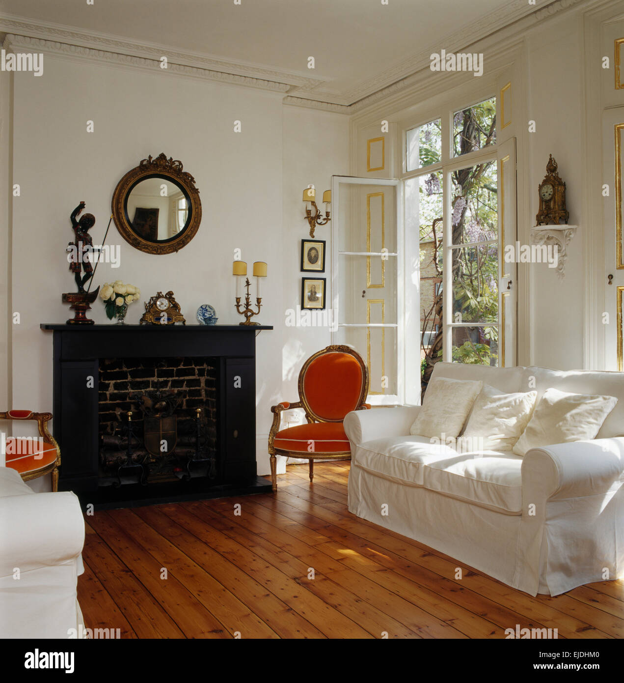 Canapés blancs et orange chaise de style français dans un cadre lumineux et spacieux salon avec cheminée en marbre noir et parquet Banque D'Images