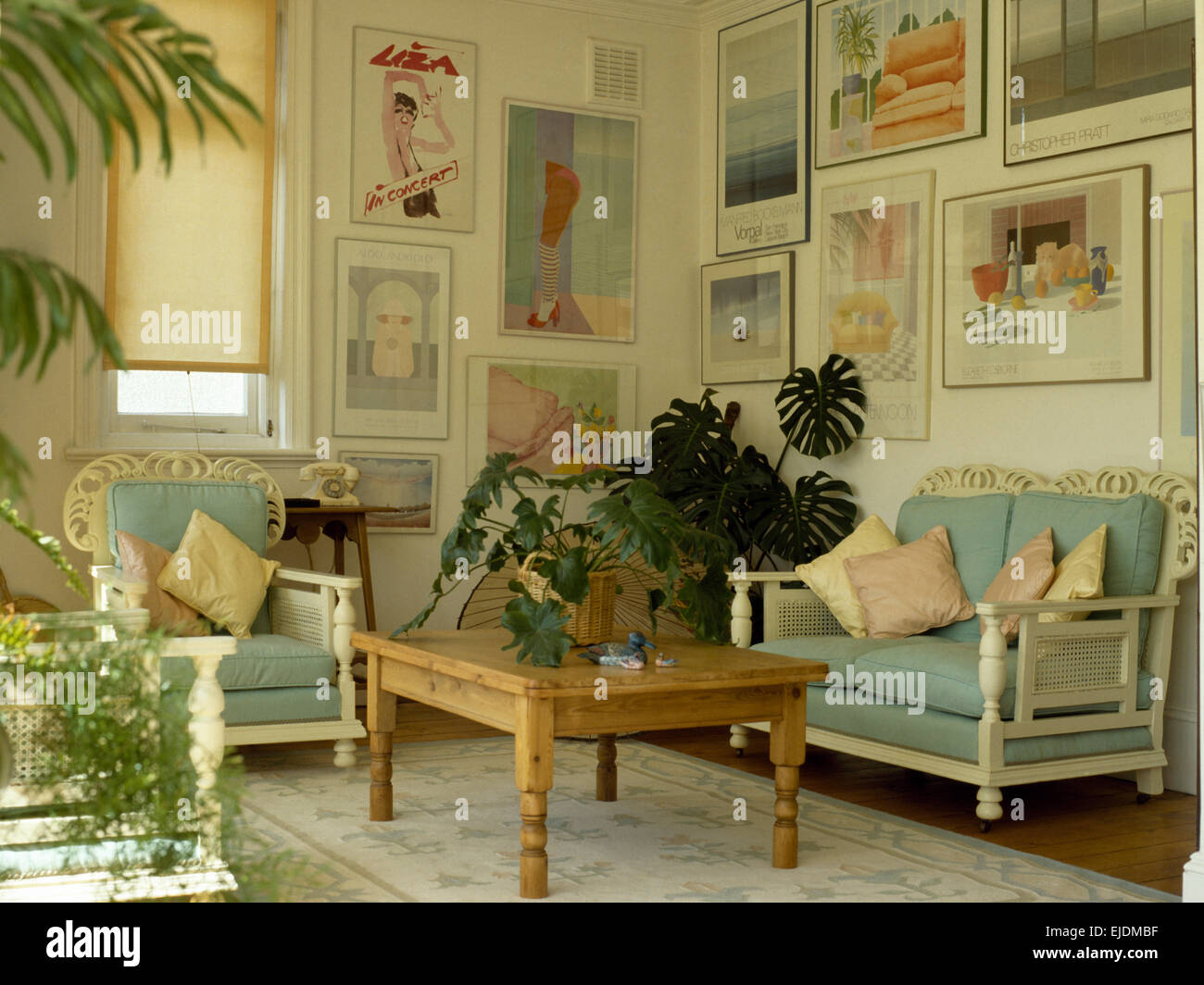 Coussins turquoise pâle sur le canapé et fauteuil en bois peint en 1980 séjour avec large affichage de posters sur les murs Banque D'Images