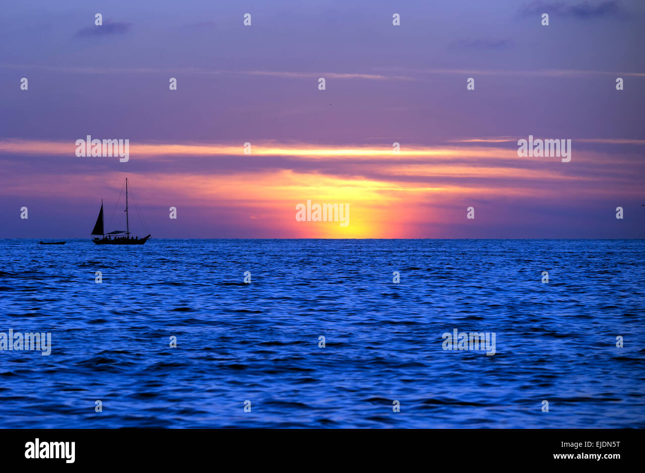 Un voilier se déplace le long de l'eau tandis que le soleil se couche à l'arrière-plan. Banque D'Images
