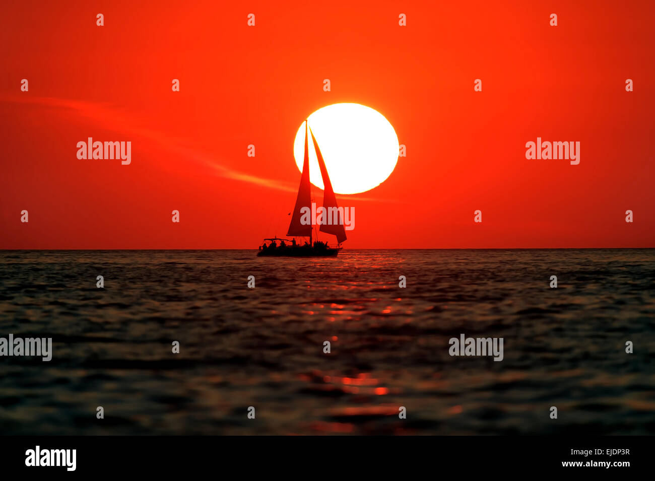 Un voilier navigue alors que le soleil se couche à l'arrière-plan. Banque D'Images
