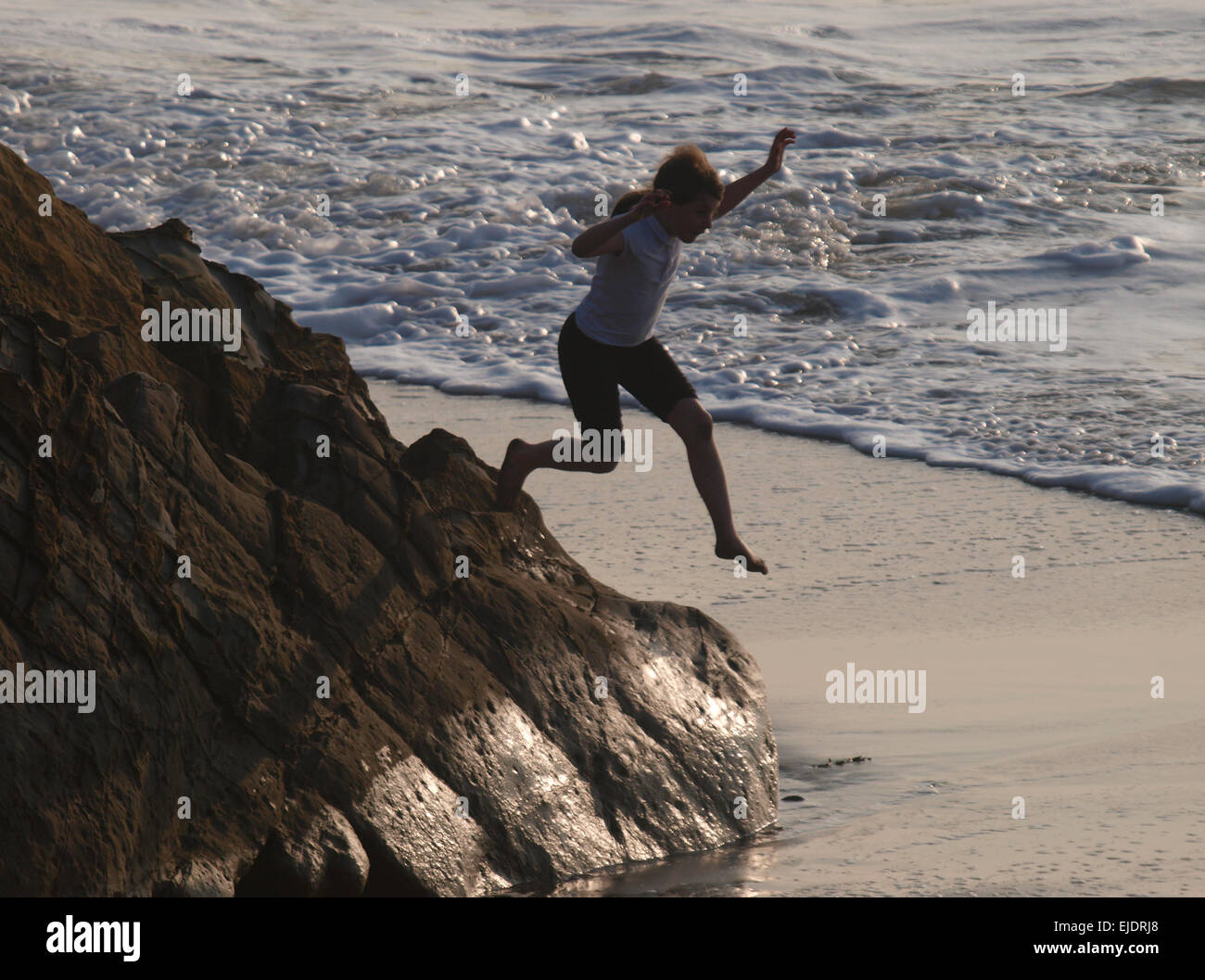 Jeune fille sauter d'un rocher au bord de la mer, lors d'une soirée à la plage, Bude, Cornwall, UK Banque D'Images