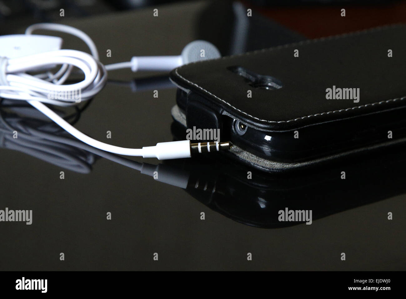 Smart phone avec prise écouteurs blanc sur noir surface de miroir Banque D'Images