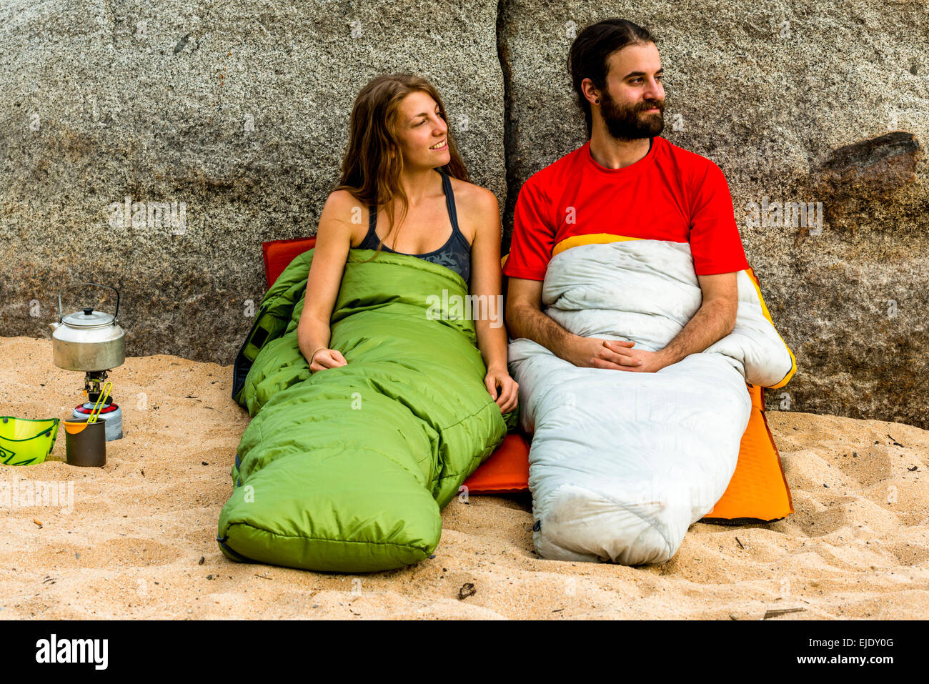 Homme et une femme sur la plage dans des sacs de couchage smiling Banque D'Images