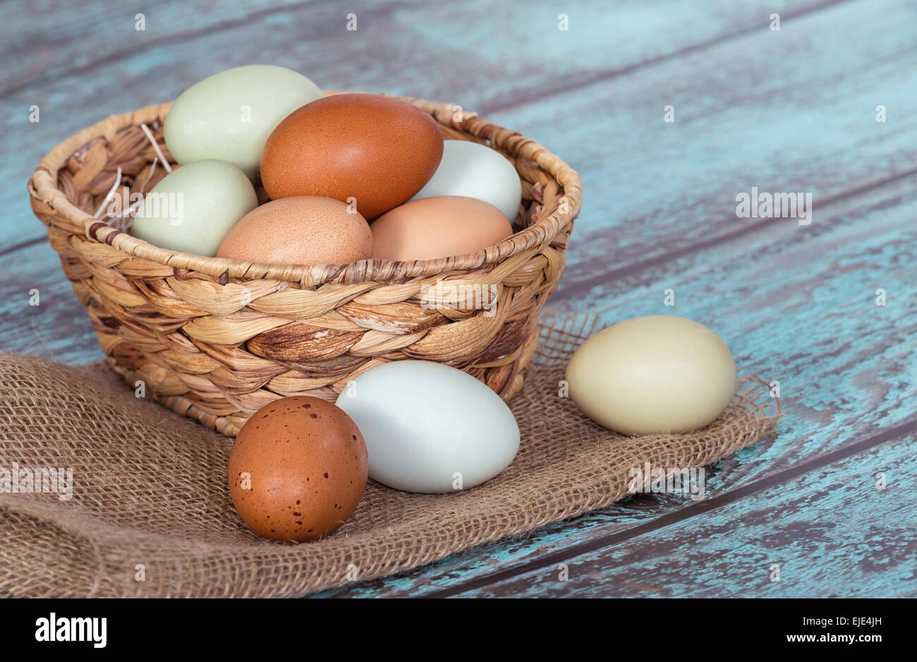 Assortiment de couleur différente, les oeufs de poulet frais dans un panier, fond vert vintage Banque D'Images