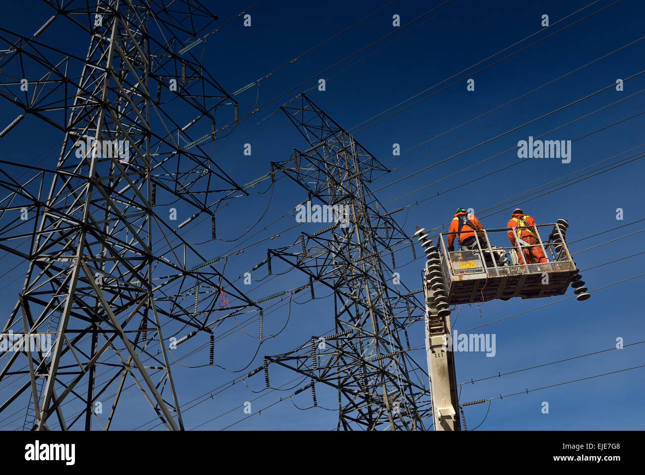 Les monteurs-hydro dans l'équipement de sécurité orange sur nacelle avec de vieux isolateurs de suspension de la ligne d'alimentation d'électricité haute tension Toronto tours on blue sky Banque D'Images