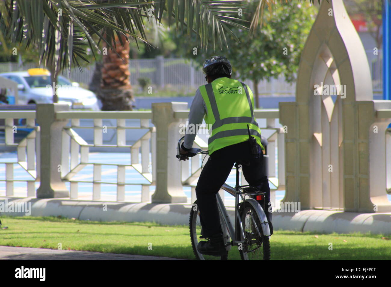Un garde de sécurité portant un gilet visible et uniforme patrouille sur son vélo dans un parc par une journée ensoleillée Banque D'Images