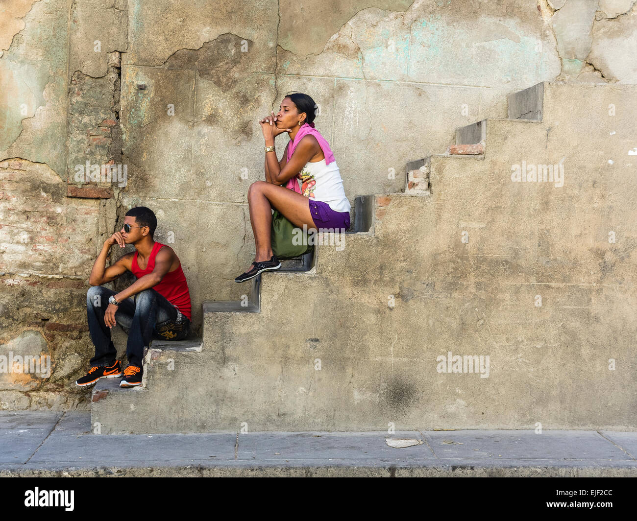 Deux personnes afro-cubaine, un homme et une femme, tous deux dans la vingtaine, installez-vous sur un escalier en béton par le côté d'une maison. Banque D'Images