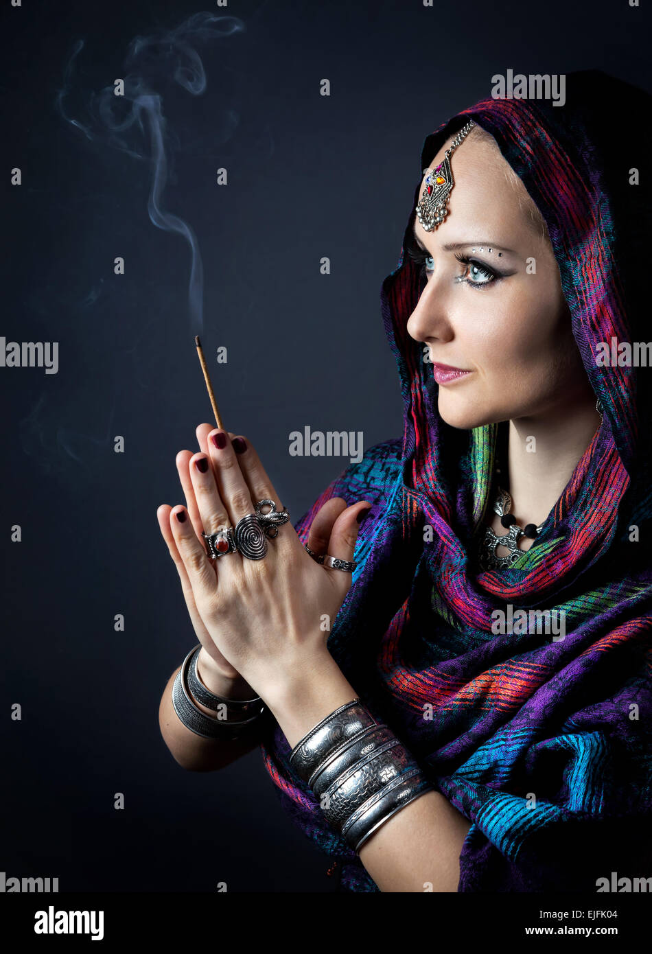 Foulard femme enveloppée dans holding bâton d'encens dans les mains à fond sombre au geste Namaste Banque D'Images