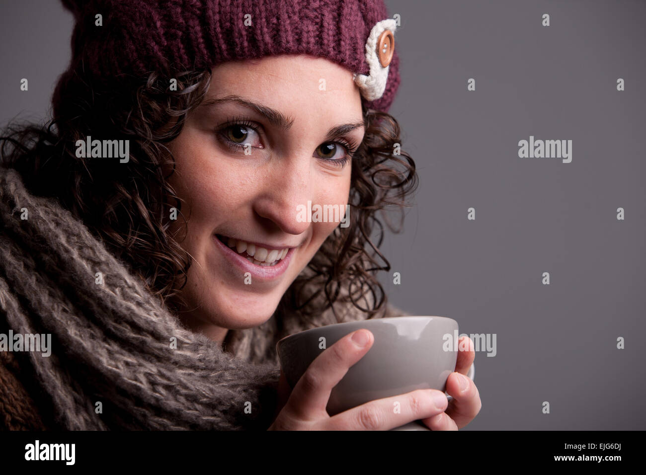 Femme souriante avec un mugful d'une boisson chaude portant des vêtements chauds comme un chapeau et un foulard Banque D'Images