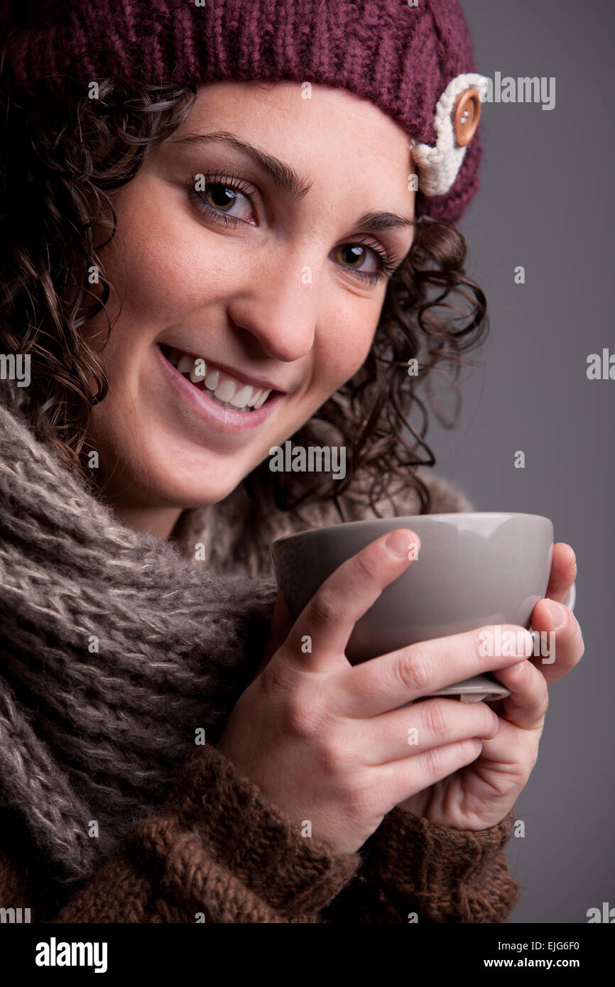 Femme souriante avec un mugful d'une boisson chaude portant des vêtements chauds comme un chapeau et un foulard Banque D'Images