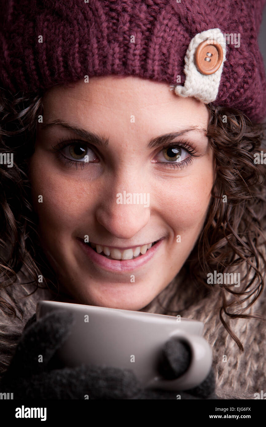 Femme souriante avec un mugful d'une boisson chaude portant des vêtements chauds comme un chapeau et un foulard Banque D'Images