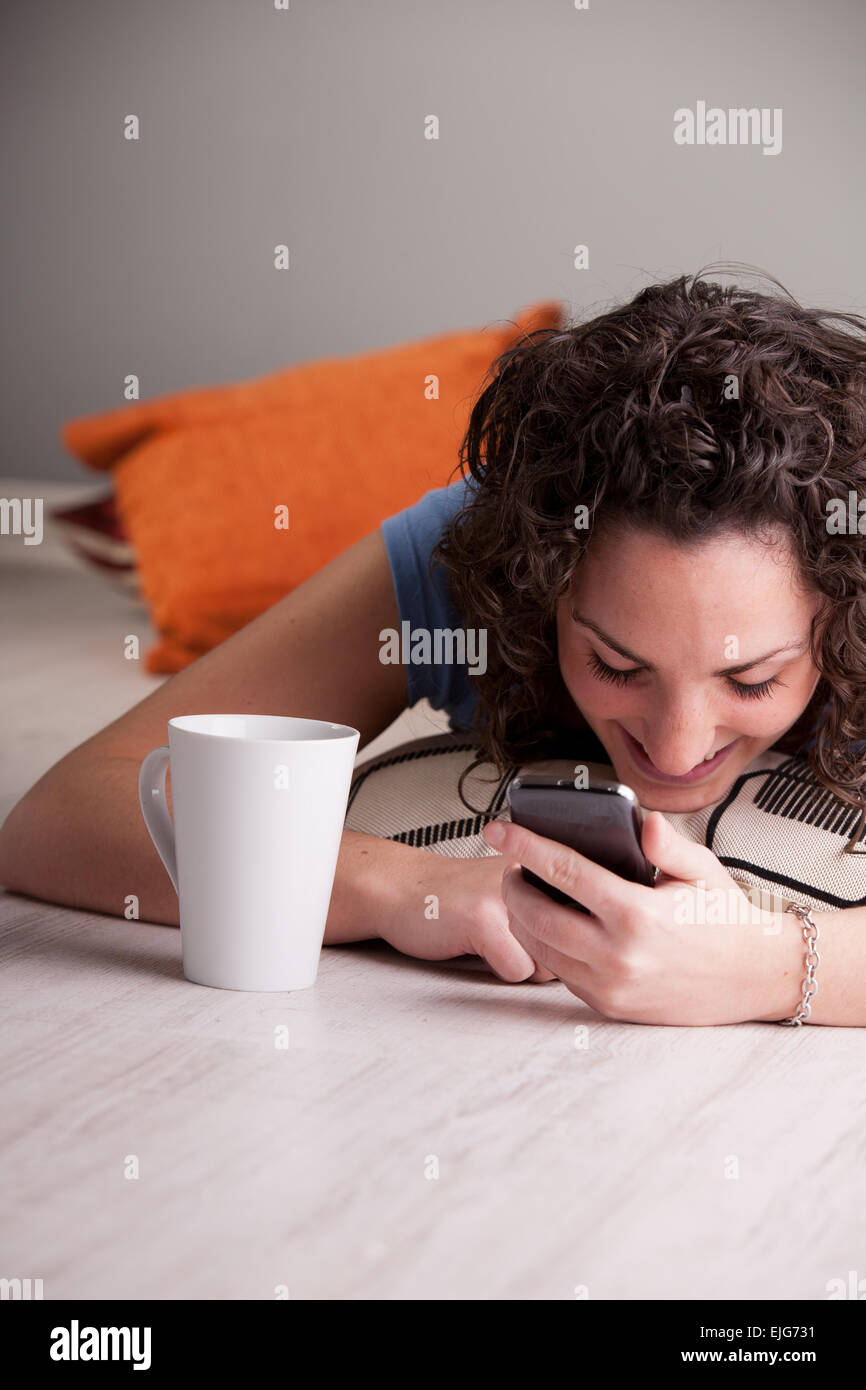 Girl enjoying son téléphone portable tout en buvant dans une tasse blanche Banque D'Images