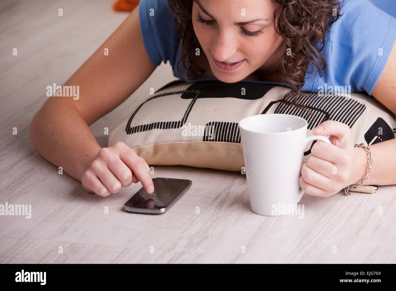 Girl enjoying son téléphone portable tout en buvant dans une tasse blanche Banque D'Images