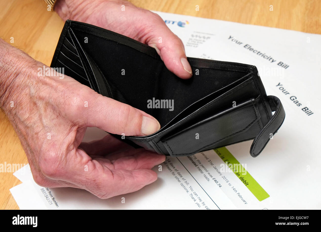 le titulaire de la pension tient un portefeuille vide ouvert avec des factures d'électricité du ménage en arrière-plan Banque D'Images