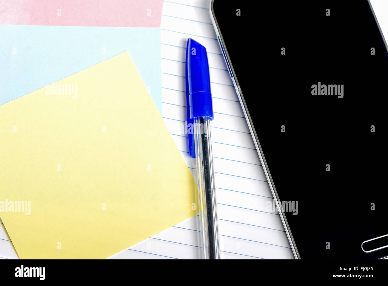Entente avec un smartphone, un stylo et du papier pour prendre des notes sur un bloc-notes, isolé Banque D'Images