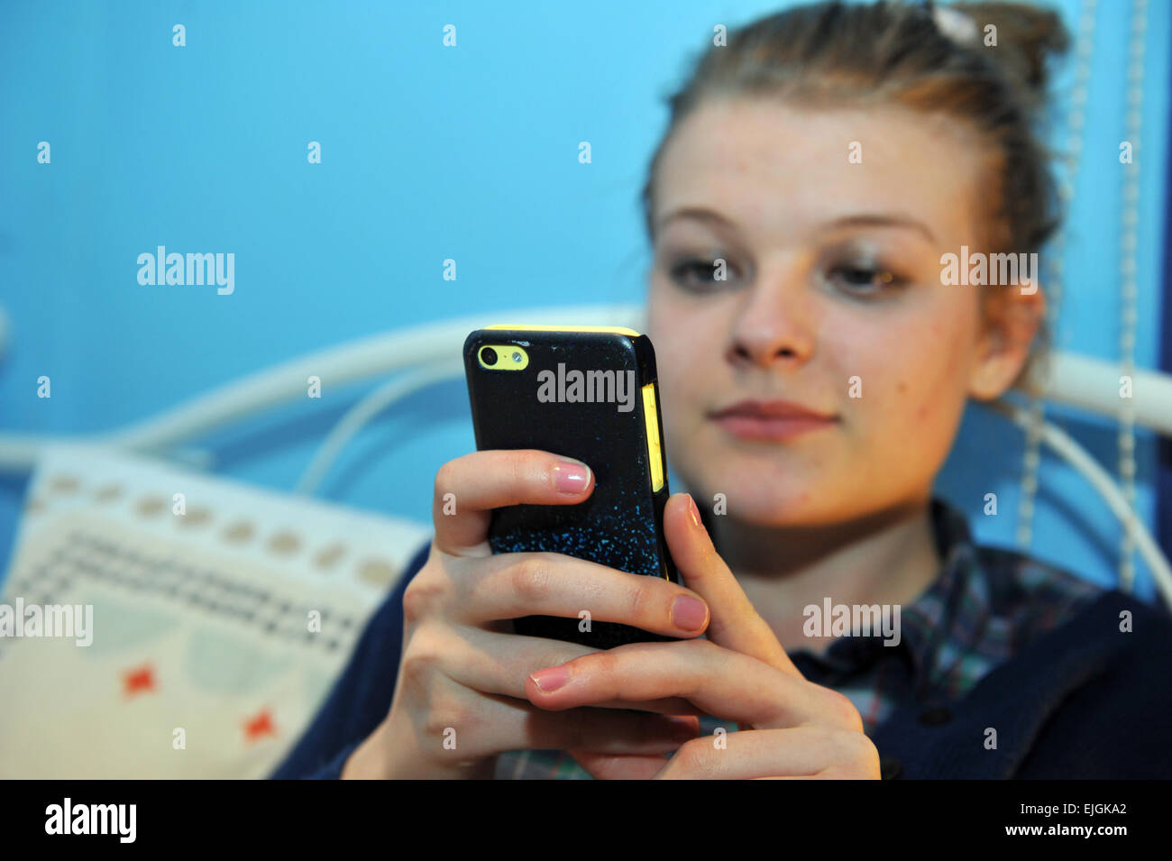 Teenage girl vérifie facebook et twitter sur son téléphone portable dans sa chambre à coucher Banque D'Images