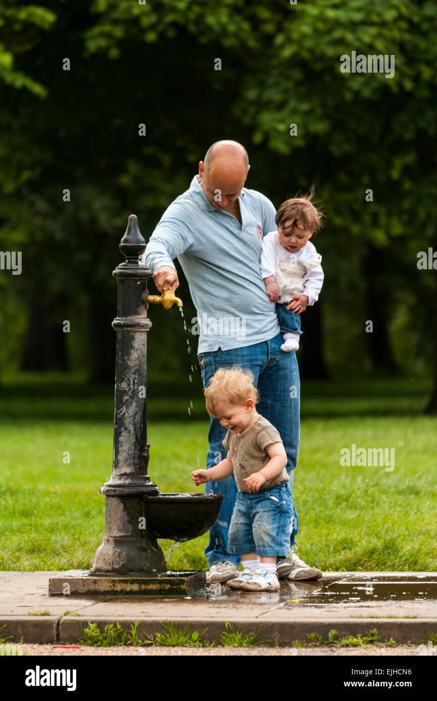 Son père et ses deux enfants à la fontaine d'eau potable à Hyde Park, Londres, Angleterre Banque D'Images