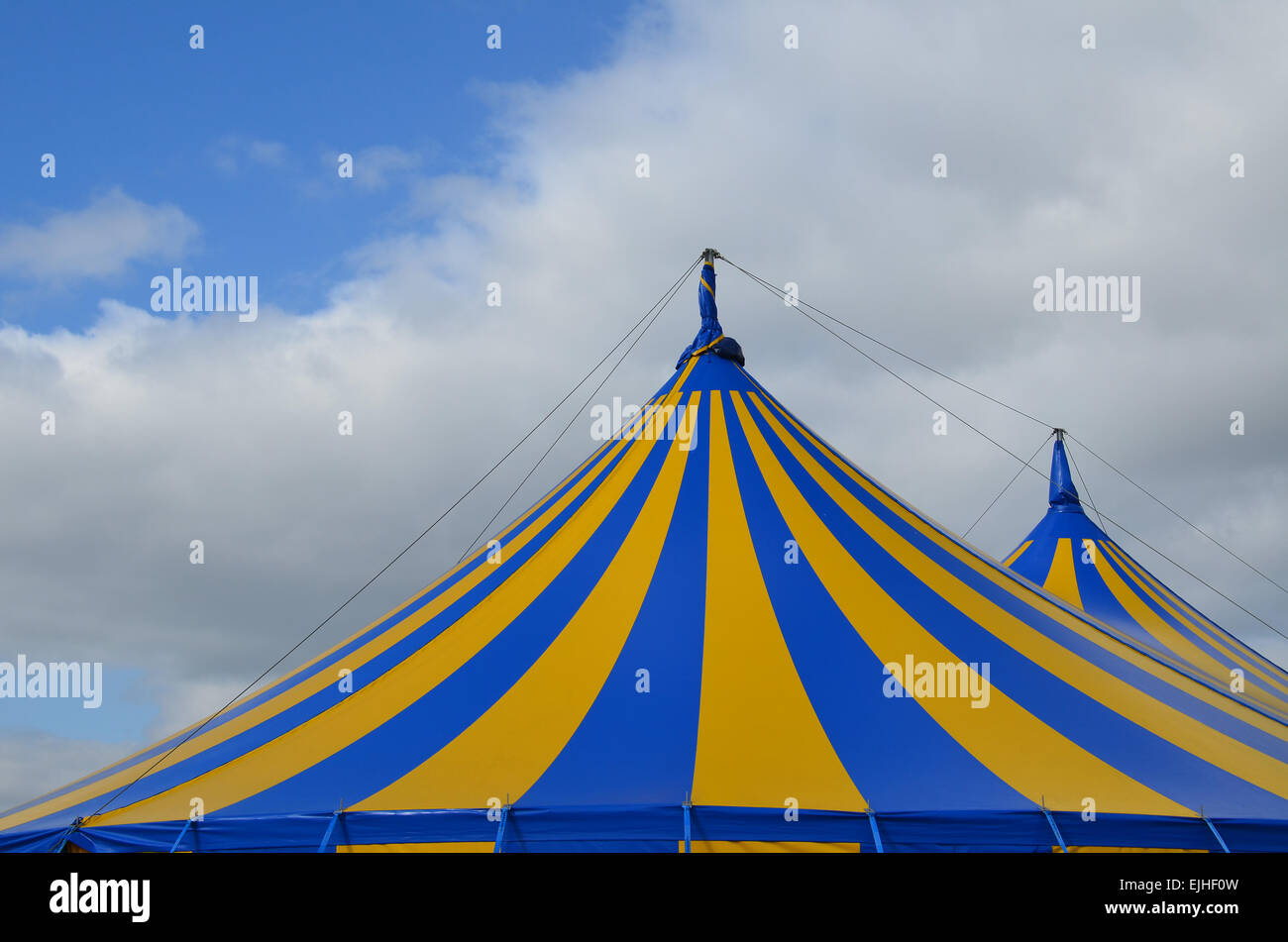 Toile rayée bleu et jaune du toit du cirque sous un ciel bleu avec des nuages blancs. Banque D'Images
