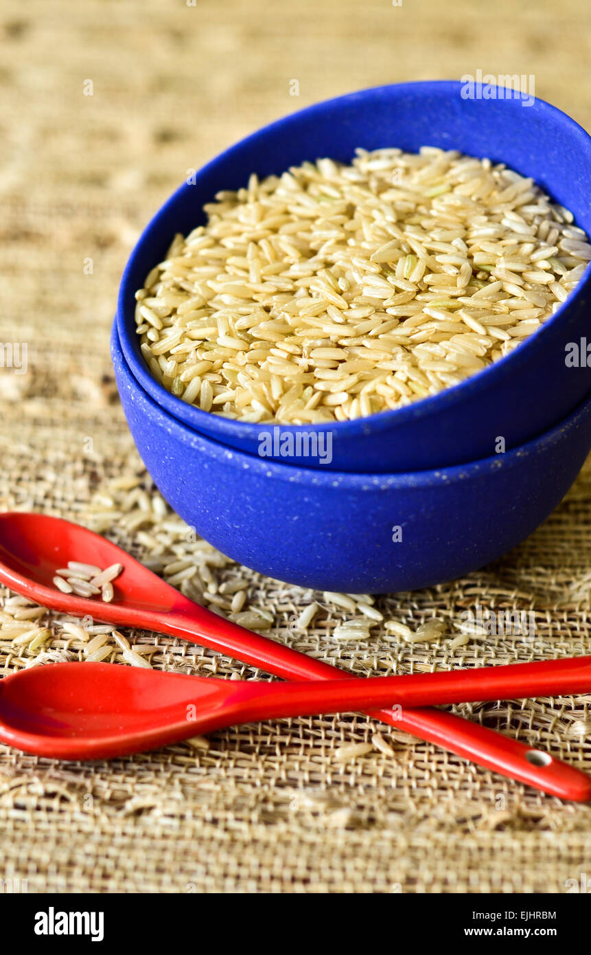 Le riz à sec dans un bol bleu et deux cuillères rouge Banque D'Images