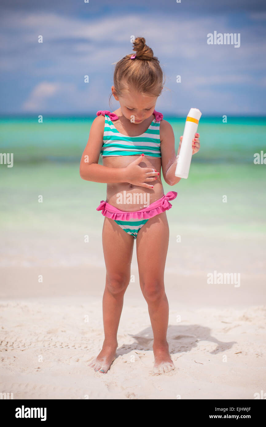 Adorable petite fille en maillot de bain avec une bouteille de lait solaire Banque D'Images