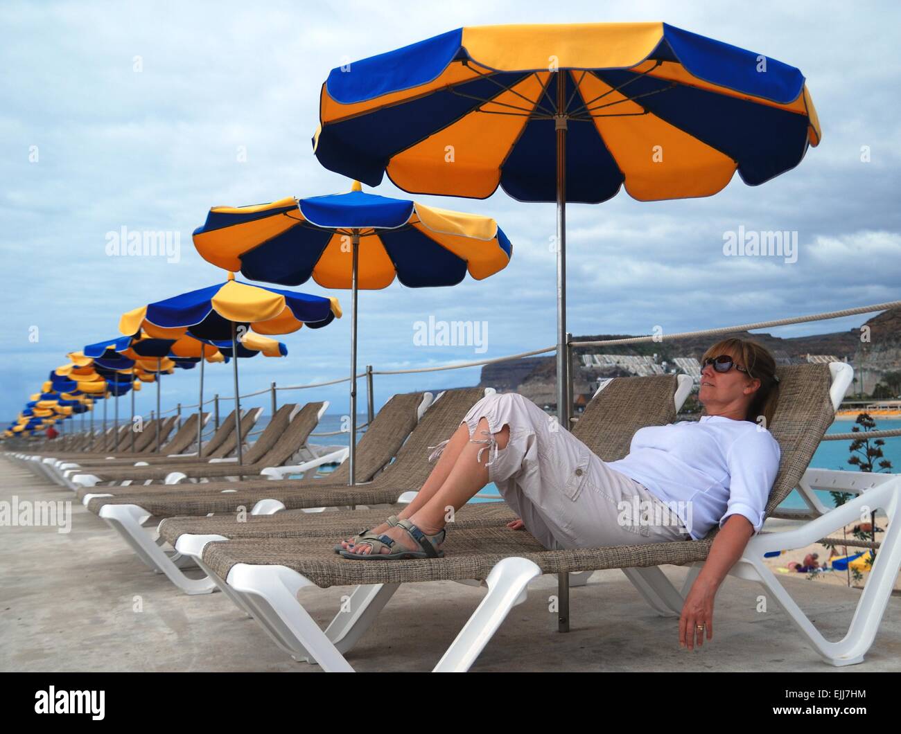 Femme couché sur un transat sous un bleu et un jaune parasol Banque D'Images