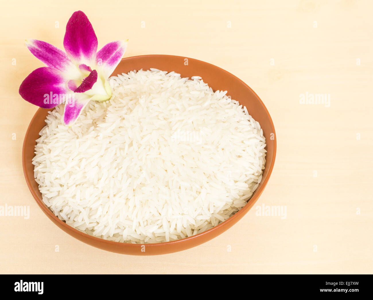 Riz au jasmin thaï parfumé dans un bol en céramique marron garnir d'orchidée, fleur sur table en bois Banque D'Images