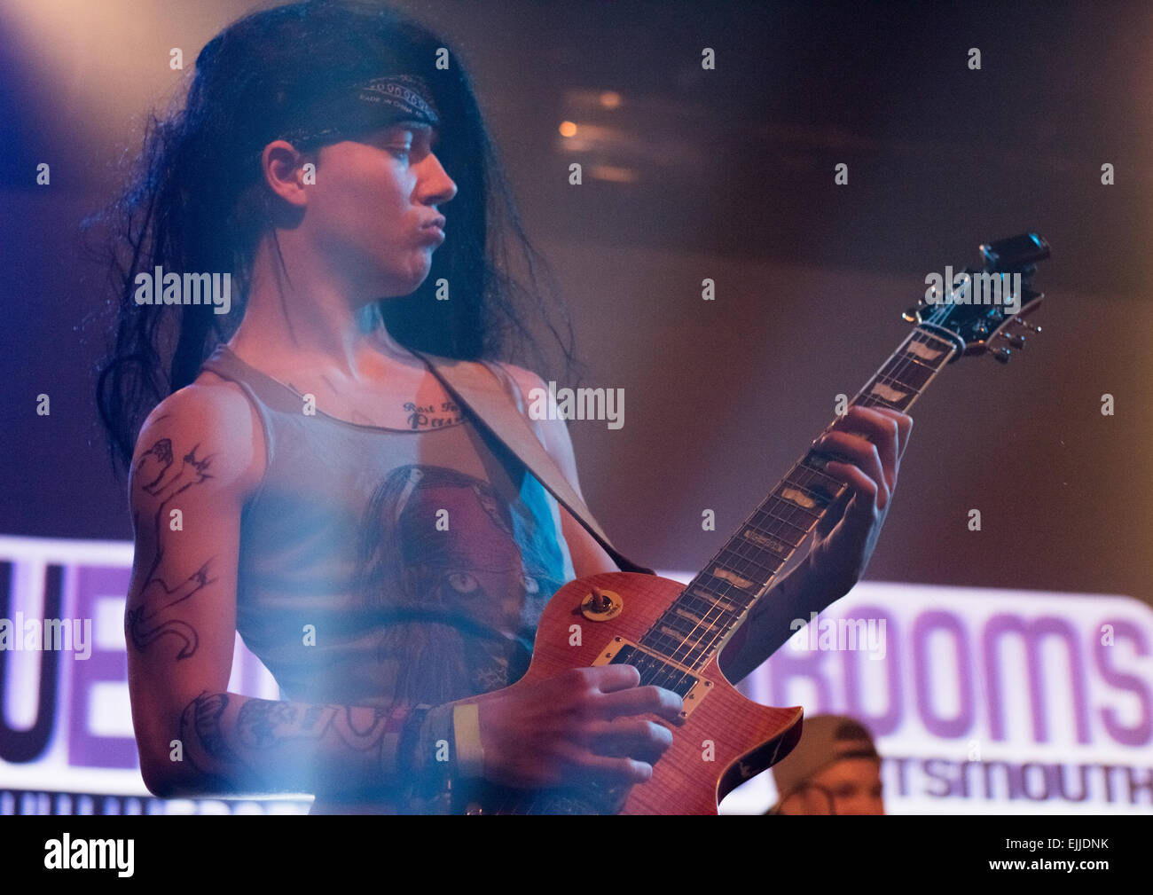 Homme guitariste d'un groupe de rock avec de longs cheveux noirs et des tatouages sur scène à un concert. Banque D'Images