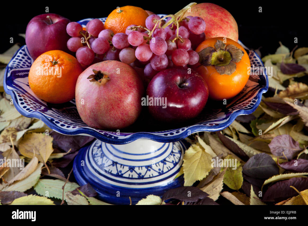 Coupe à fruits en céramique avec fruits d'automne sur fond noir isolé. Pleine Surface de feuilles sèches Banque D'Images