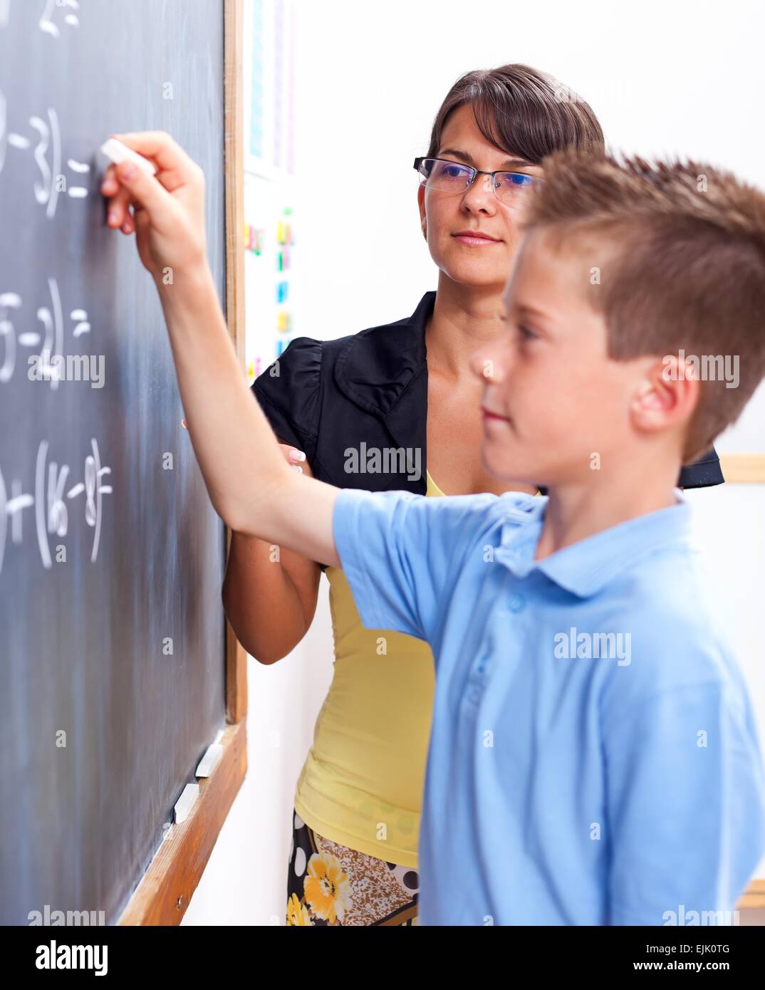 Boy standing in front of chalkboard, résoudre l'équation, en face de l'enseignant Banque D'Images