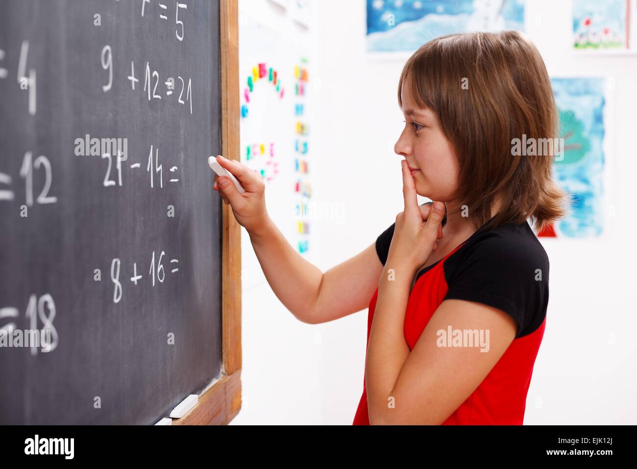 Elementary School Girl standing in front of chalkboard et réflexion sur la solution des équations mathématiques Banque D'Images