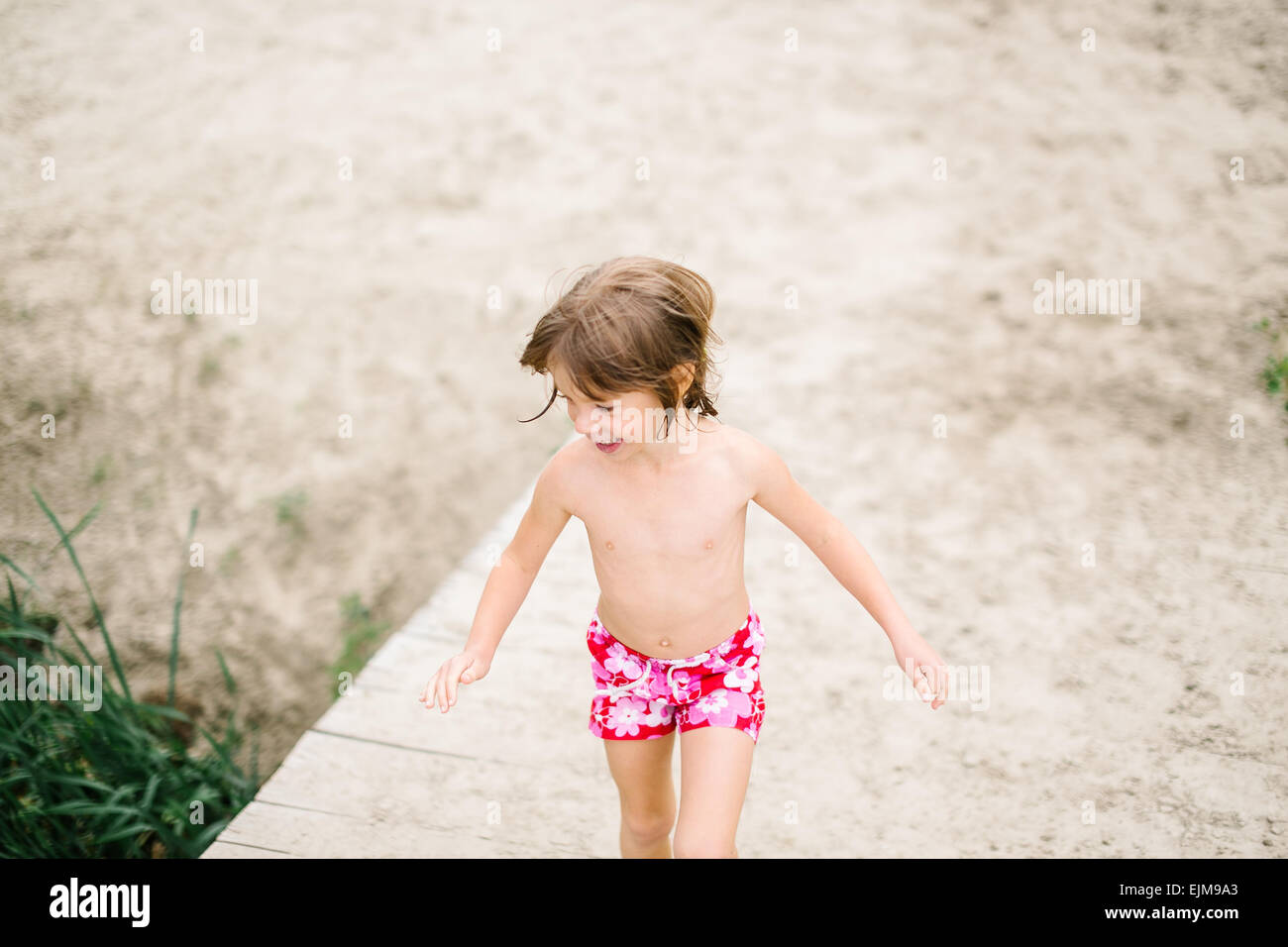 Petite fille à la plage sur chaude journée d'été. S'amuser durant les vacances. Fille qui marche sur la terrasse en bois au bord du lac Banque D'Images
