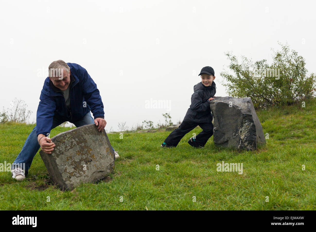 Hauts homme et enfant garçon d'essayer de déplacer gros rochers à l'extérieur. Banque D'Images