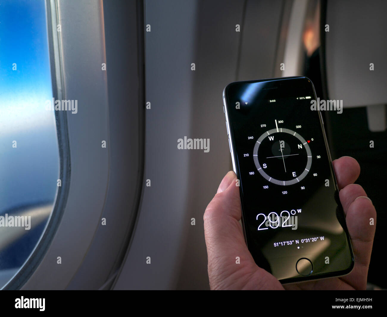 Main du SMARTPHONE COMPASS tenant le smartphone iPhone 6 affichant la  boussole et la direction de l'application de vol à l'écran, l'aile de la  fenêtre de cabine et le ciel derrière Photo