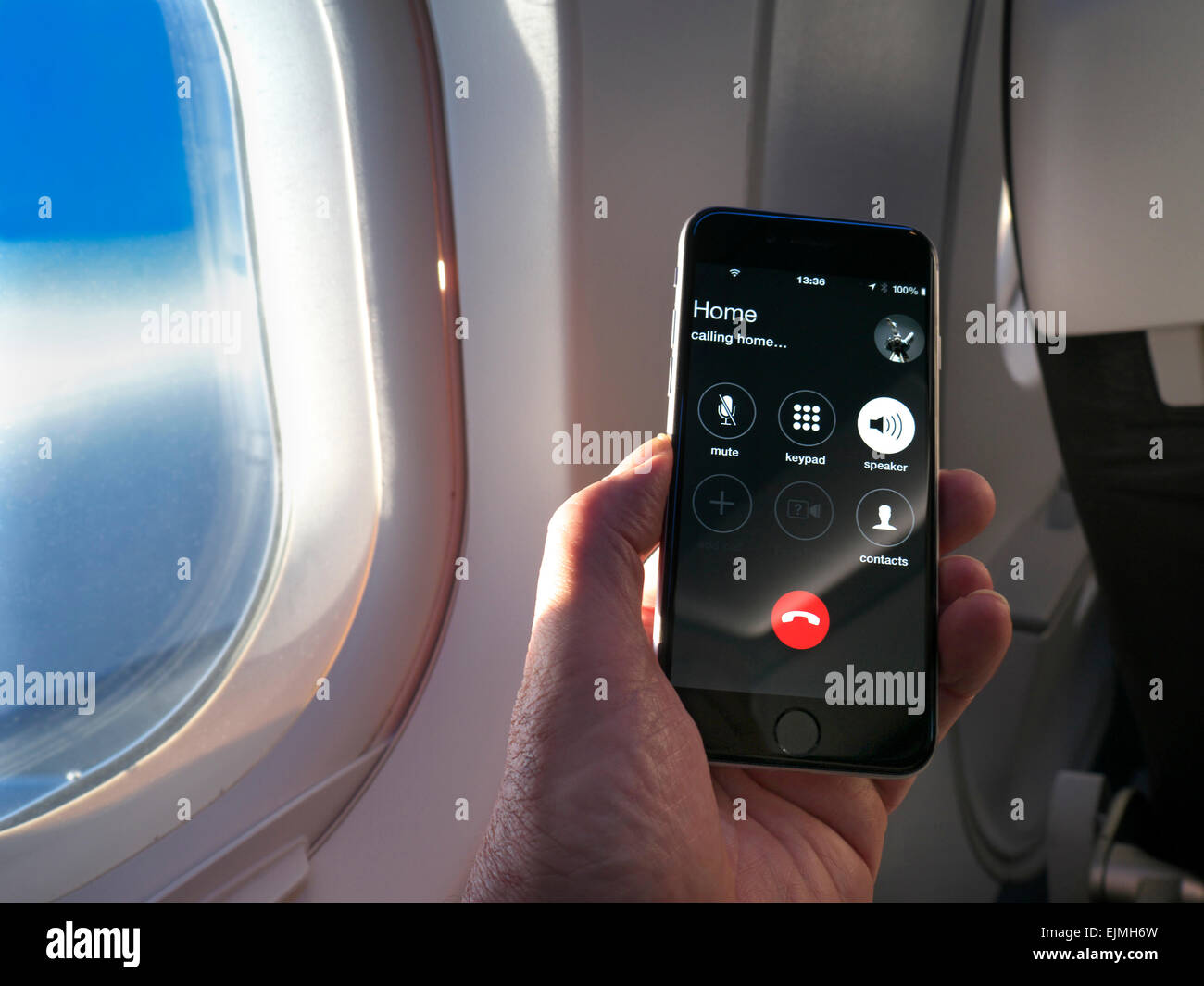 Smartphone iPhone portable avec écran d'appel « home » en vol, avec aile de fenêtre de cabine et ciel bleu derrière Banque D'Images
