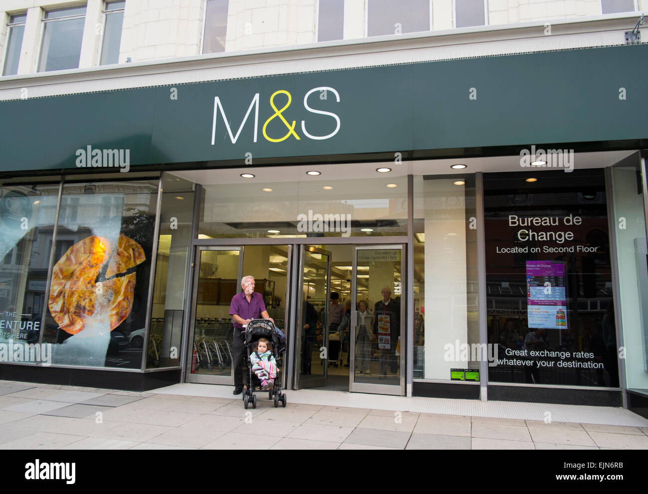 Un homme Senior citizen avec bébé en poussette laisse un magasin Marks and Spencer à Llandudno, au Pays de Galles, Royaume-Uni Banque D'Images