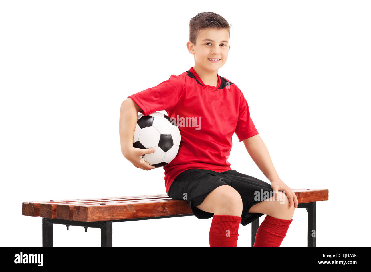 Fier un joueur de football junior posant assis sur un banc en bois et la tenue d un football dans sa main isole sur fond blanc Photo Stock Alamy