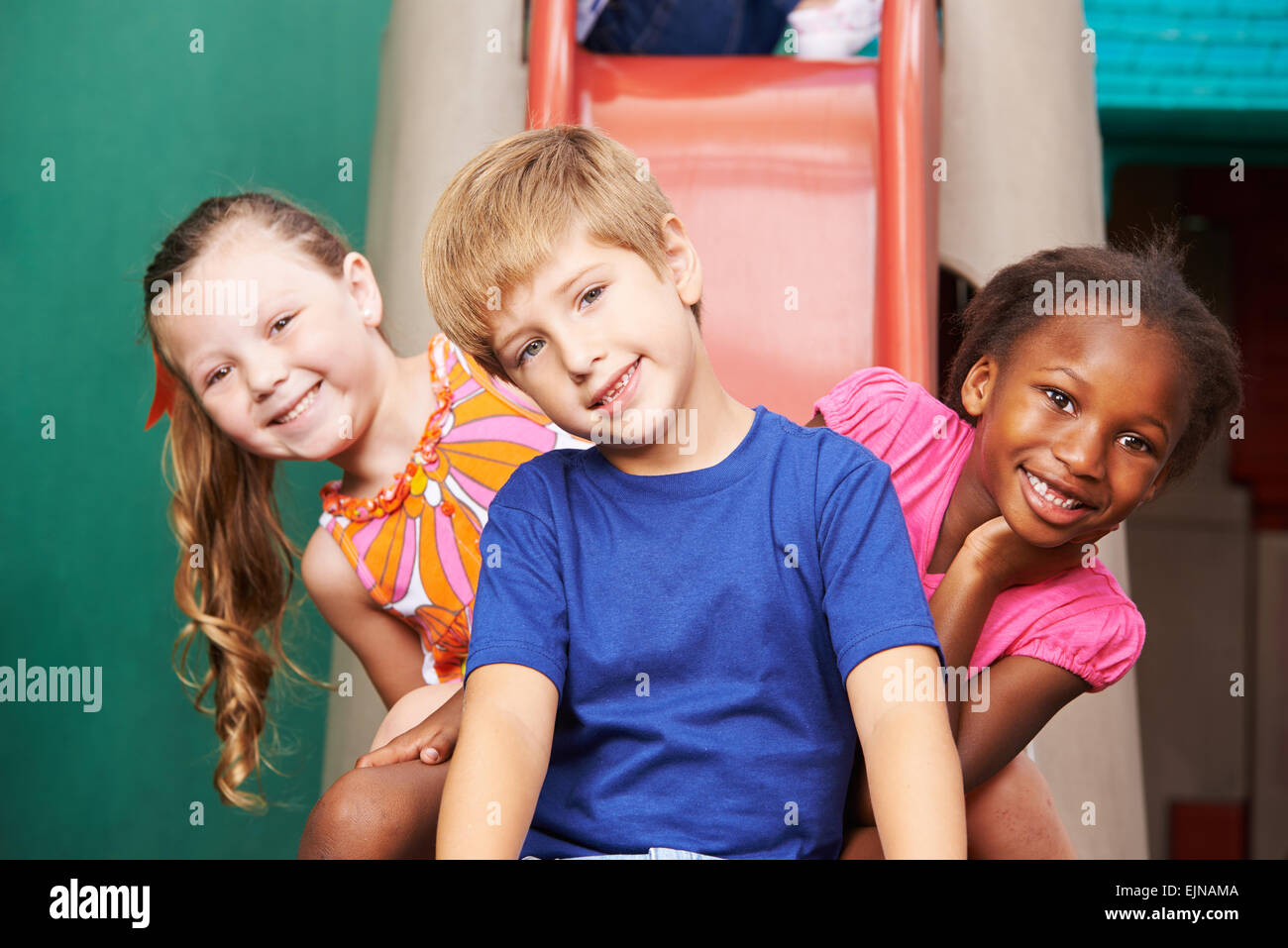 Trois enfants heureux assis sur une diapositive de la maternelle Banque D'Images