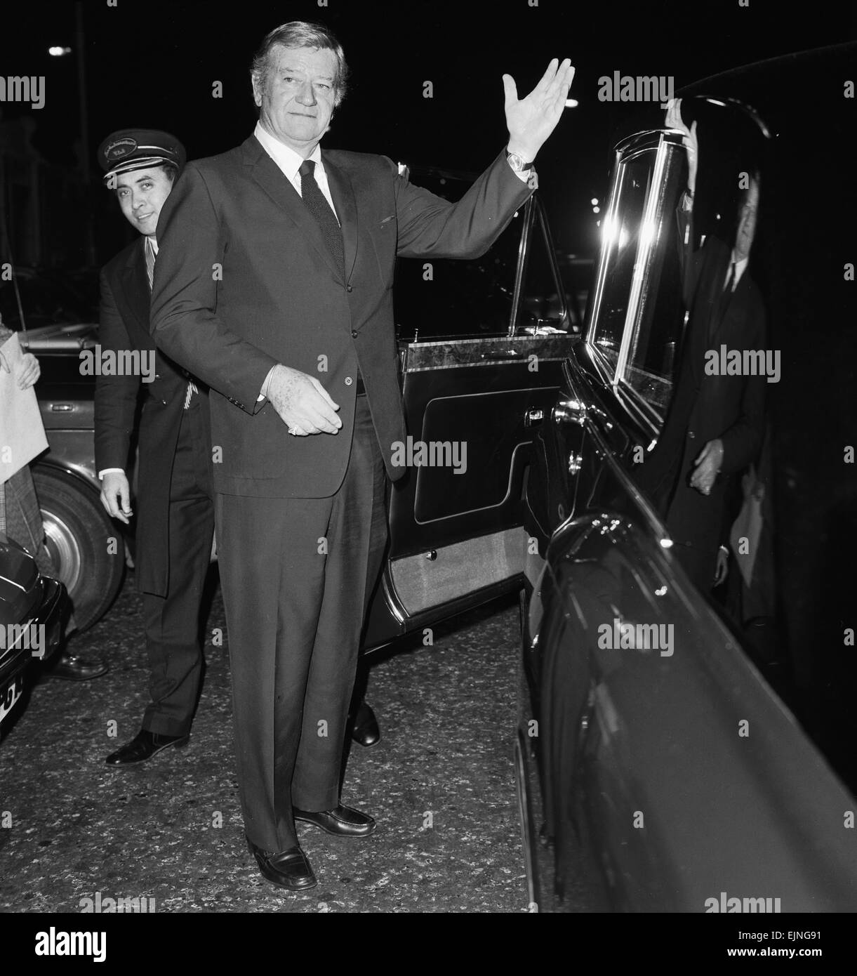 L'acteur américain John Wayne laissant les Ambassadeurs Club à Hamilton, London regardé par portier Tas d'aulnes. 17 janvier 1974. Banque D'Images