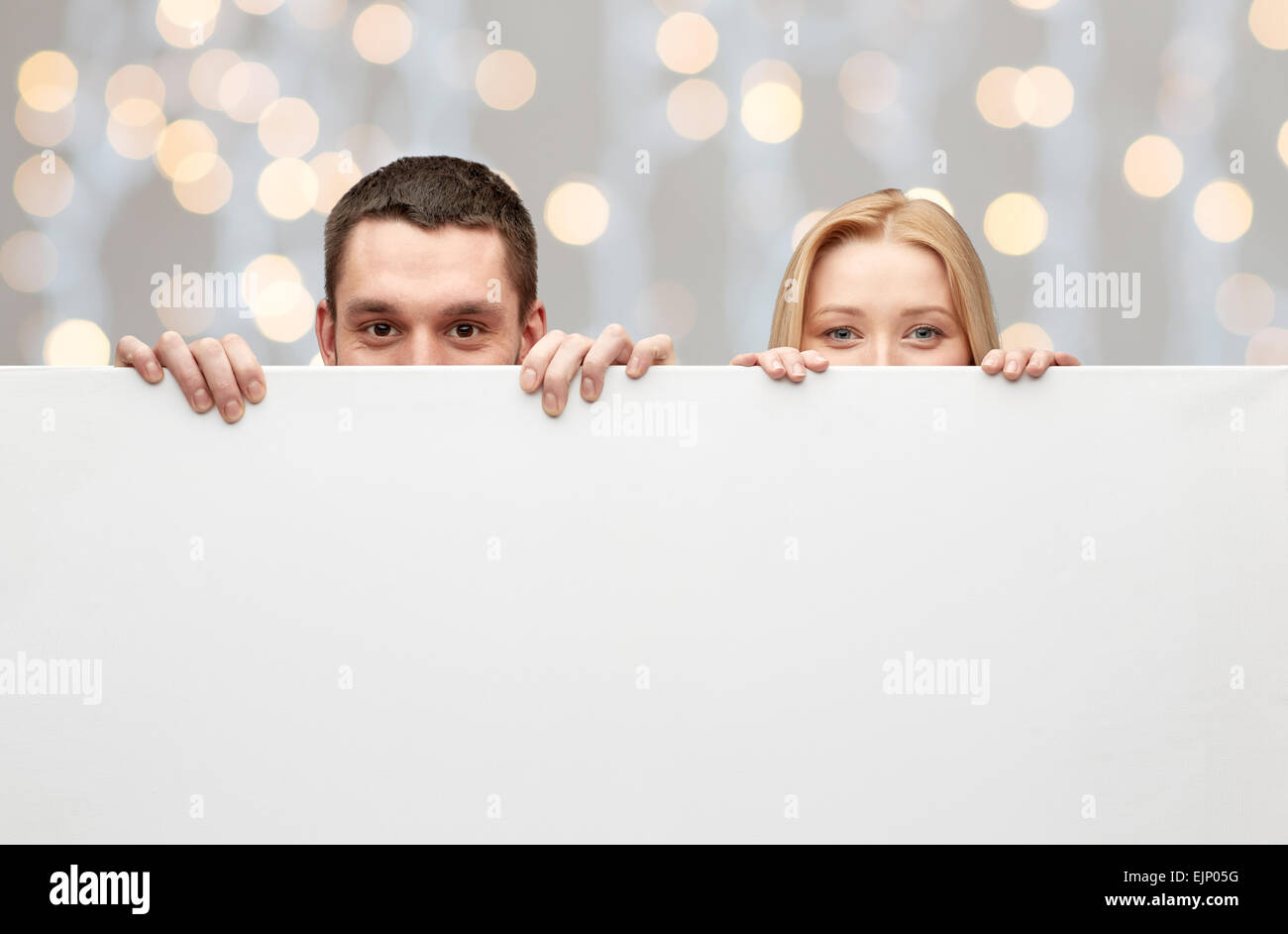 Couple heureux se cacher derrière big white blank board Banque D'Images