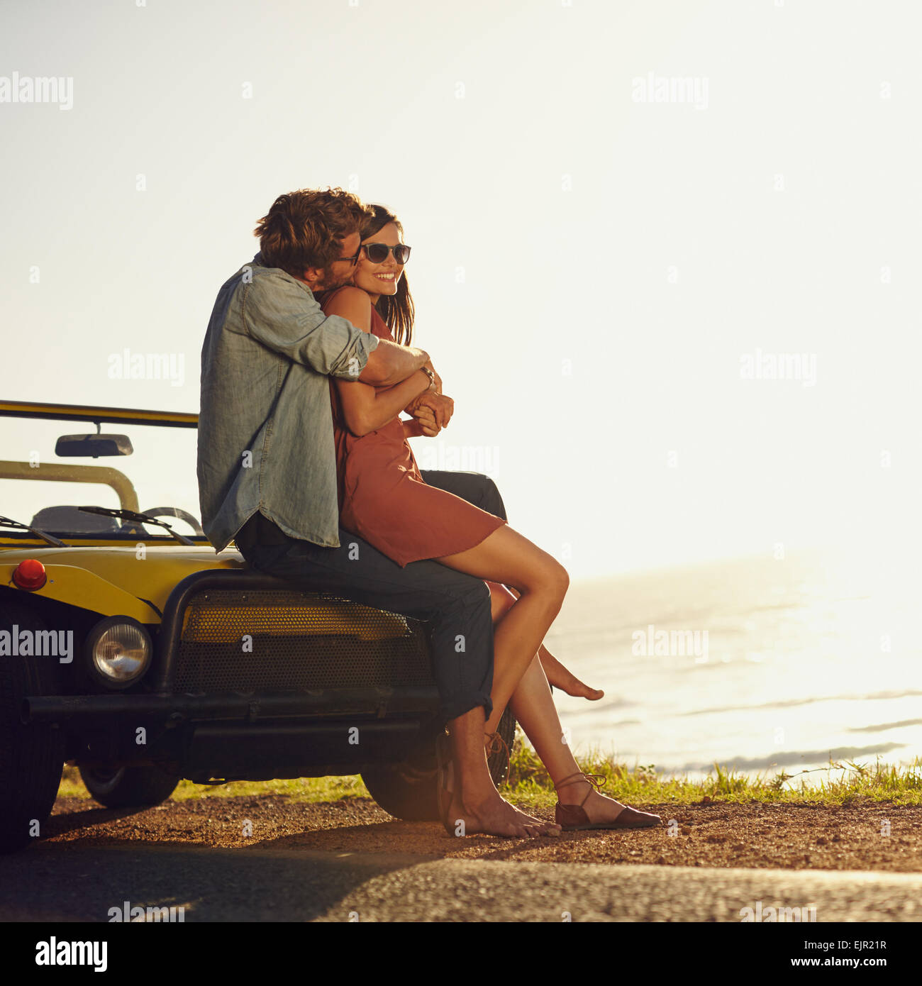Jeune couple dans l'amour et faire place au baiser. Jeune homme et femme assis sur son capot de voiture. Couple on road trip. Banque D'Images