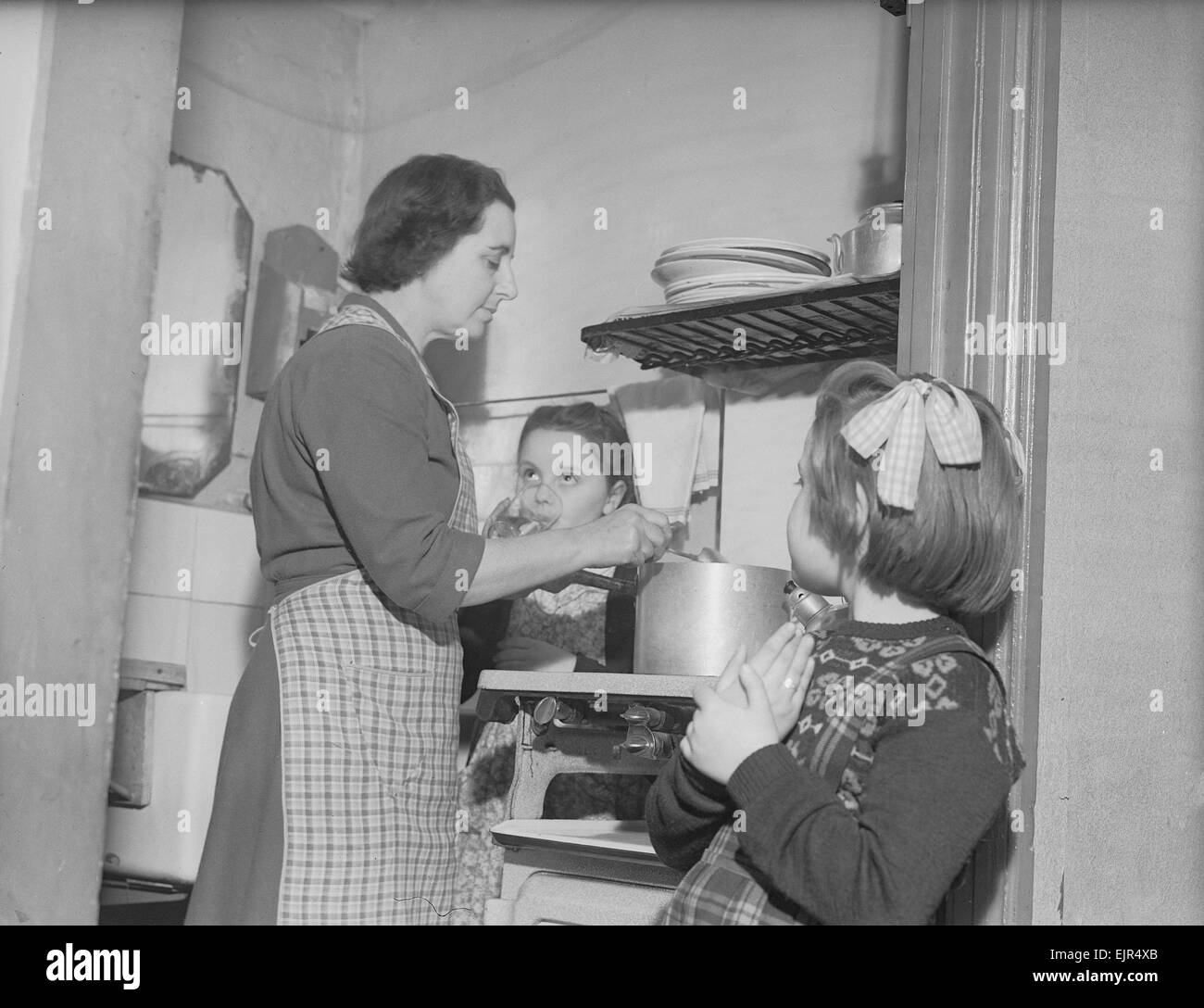 Rester à la maison mère Mme Mary Mackenzie vu préparer le repas du soir sous surveillance par ses deux filles Linda et Dau. 2 novembre 1952 Banque D'Images