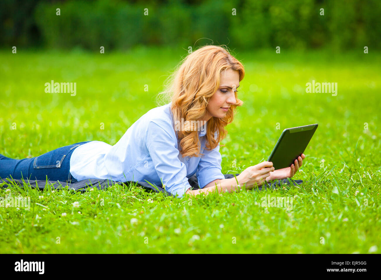 Belle blonde woman lying in grass et à l'aide d'une tablette Banque D'Images