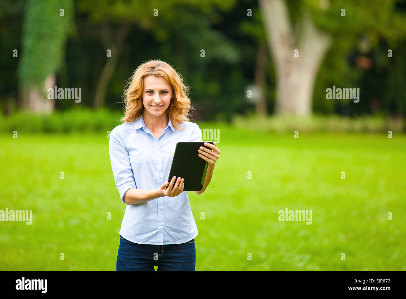 Belle jeune femme avec le comprimé dans la main, en marchant dans le parc Banque D'Images