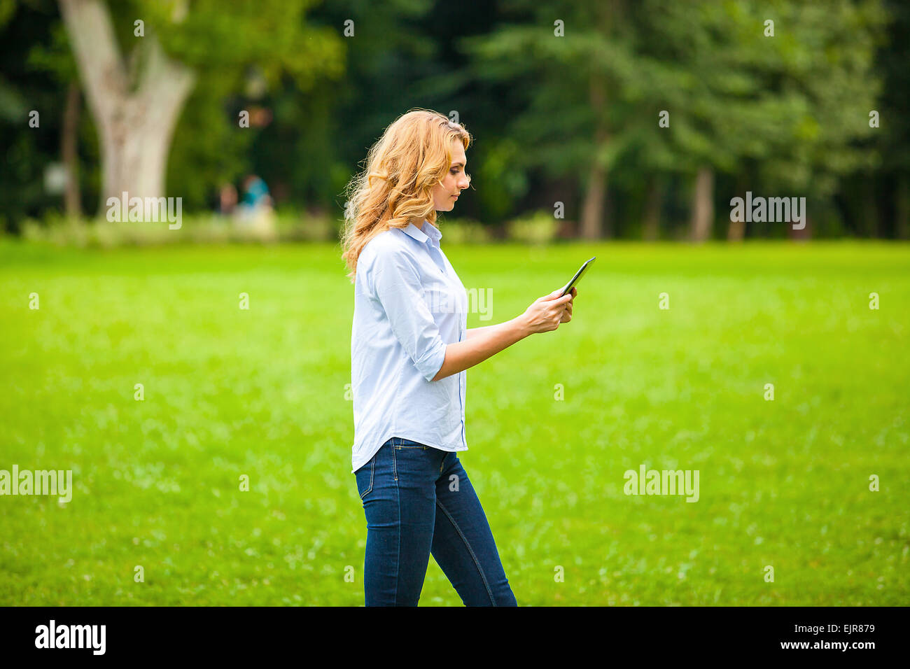 Belle jeune femme avec le comprimé dans la main, en marchant dans le parc Banque D'Images